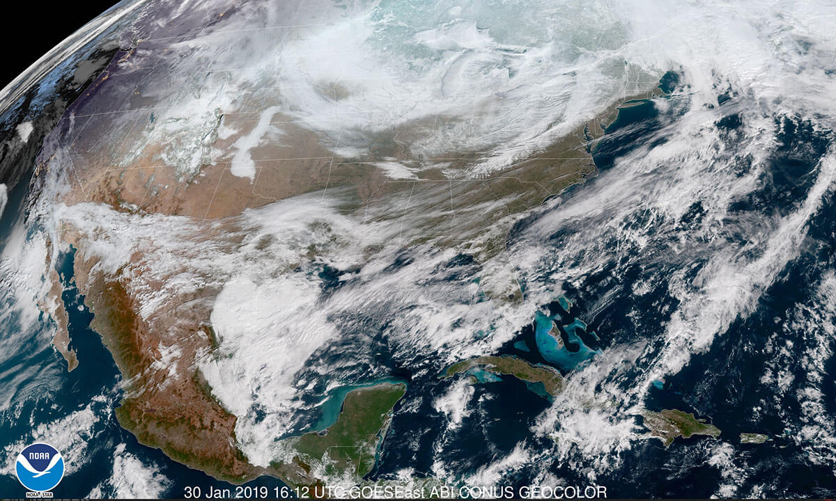 An image of Earth from a satellite shows white clouds being blown by arctic winds across the tan and green land of the United States.