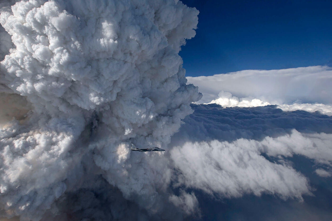 Large clouds of smoke with a jet flying in front of them.