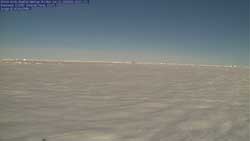 Flat, snow-covered expanse with horizon and sunny blue sky above.