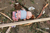 Photo of doll lying on ground surrounding by scraps of debris. 