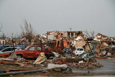 A tornado has left a pile of bricks, lumber, and other house debris along with twisted and ruined cars.