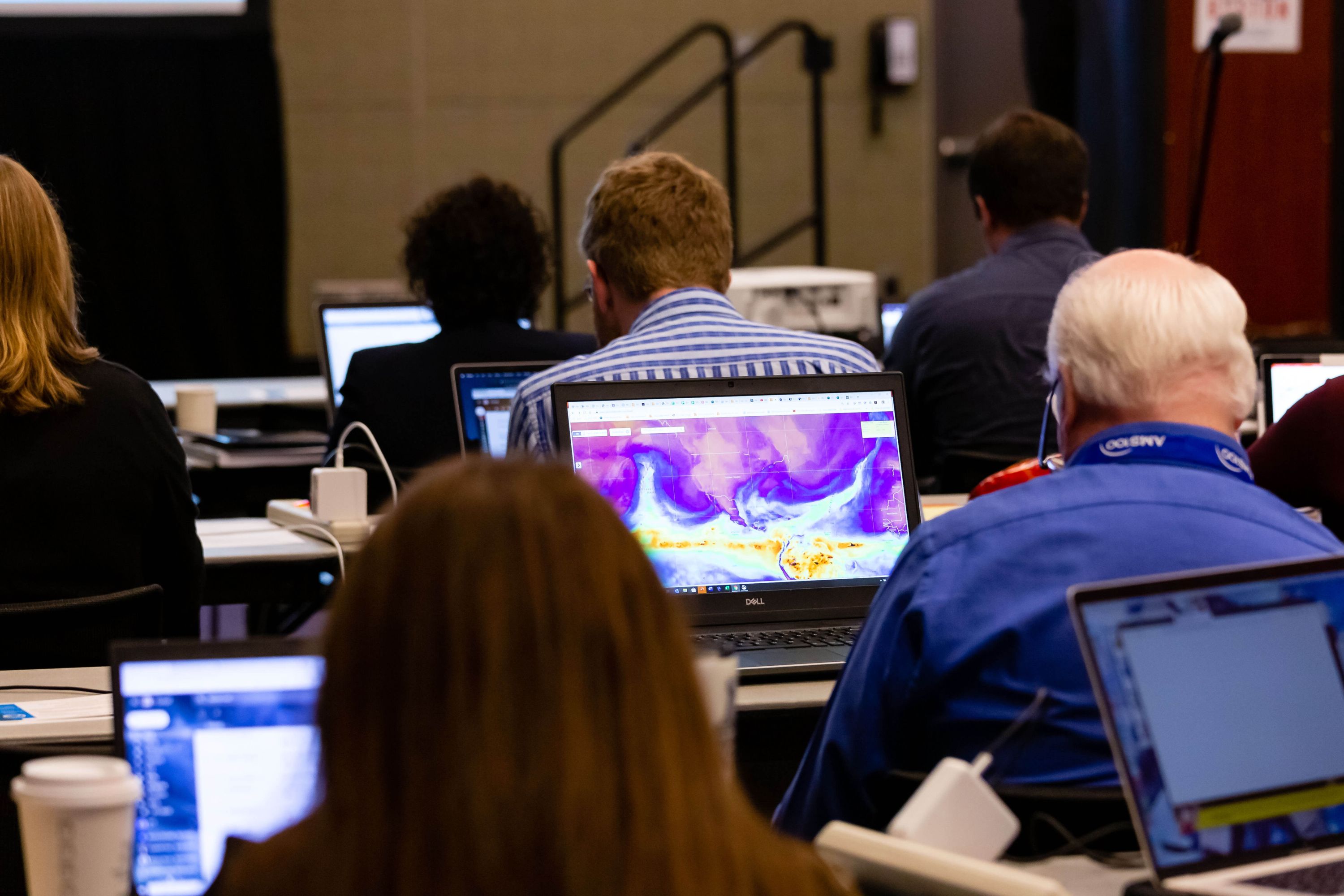 A photograph of people in a room, each sitting at a desk facing forward and working on a computer.