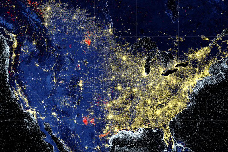 This image is a composite night-time view of the United States from space, showing various sources of light. The U.S. is outlined with the lights of cities and towns, and the vast darkness of the oceans contrasts with the illuminated areas. Red dots indicate natural gas flares, gold dots indicate artificial light, and white dots indicate boat detections. 