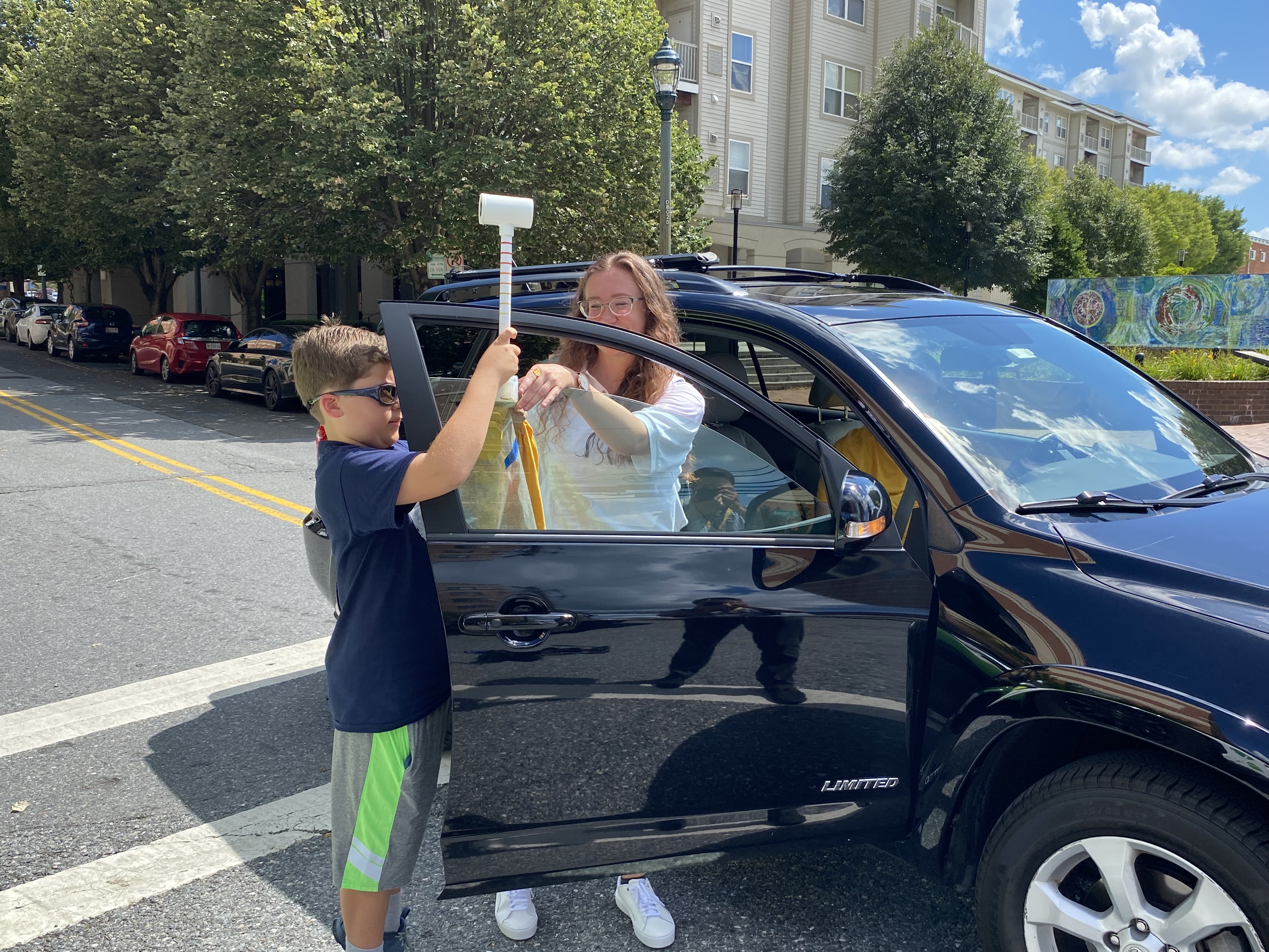A woman and boy with a camera standing outside of a car.