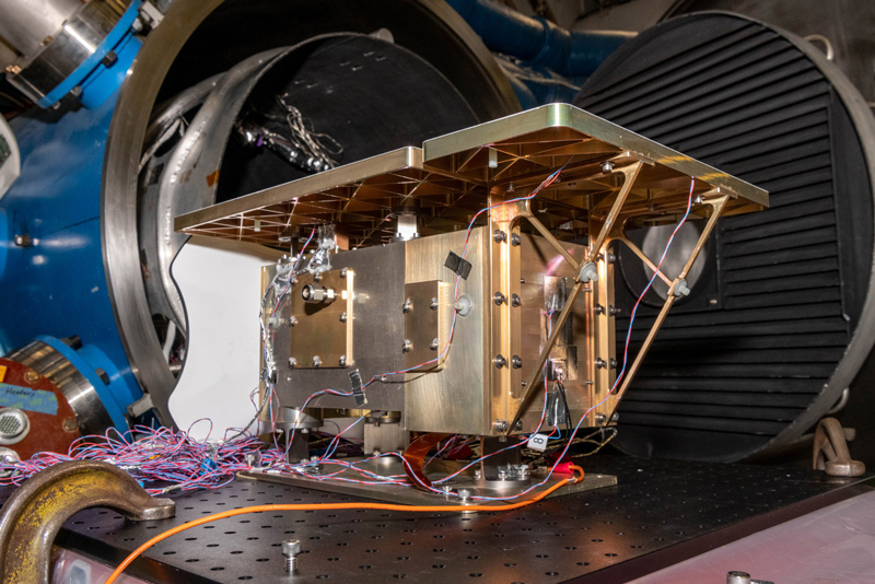 HARP2 instrument undergoing thermal vacuum testing, with wiring and components exposed, set against large testing machinery in a laboratory environment.
