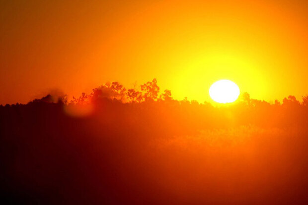 An image shows a vibrant sunset with a glowing orange sun near the horizon, silhouetting trees and casting warm hues across the sky and landscape.