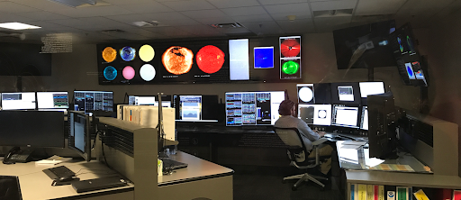 People in front of a several computer screens.