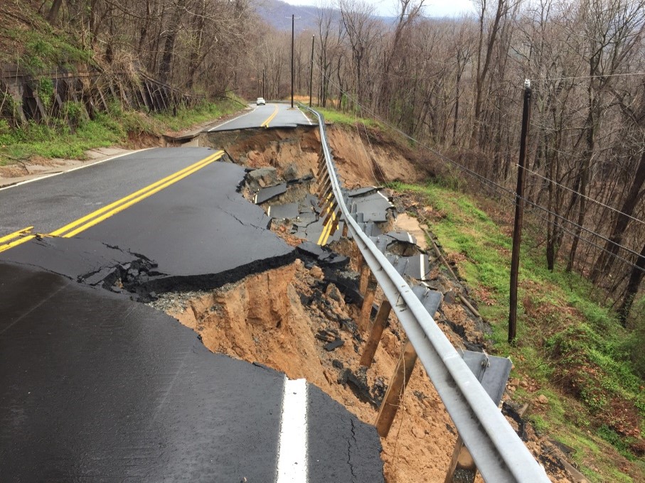 A severely damaged roadway with collapsed pavement and guardrails due to significant erosion and landslide, making it completely impassable.