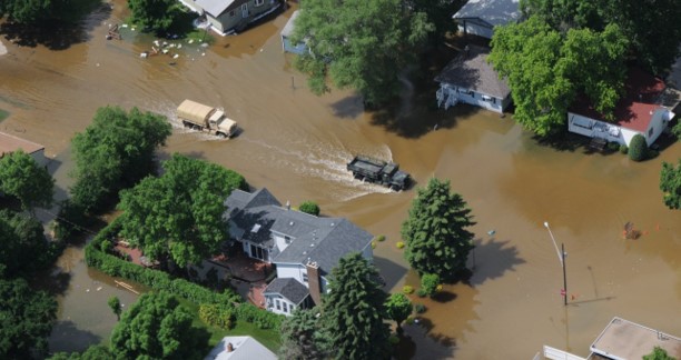 Trucks and buildings with brown flood waters around it.