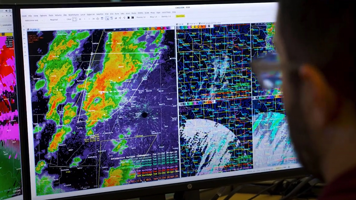 A meteorologist looks at a computer screen displaying weather data imagery.