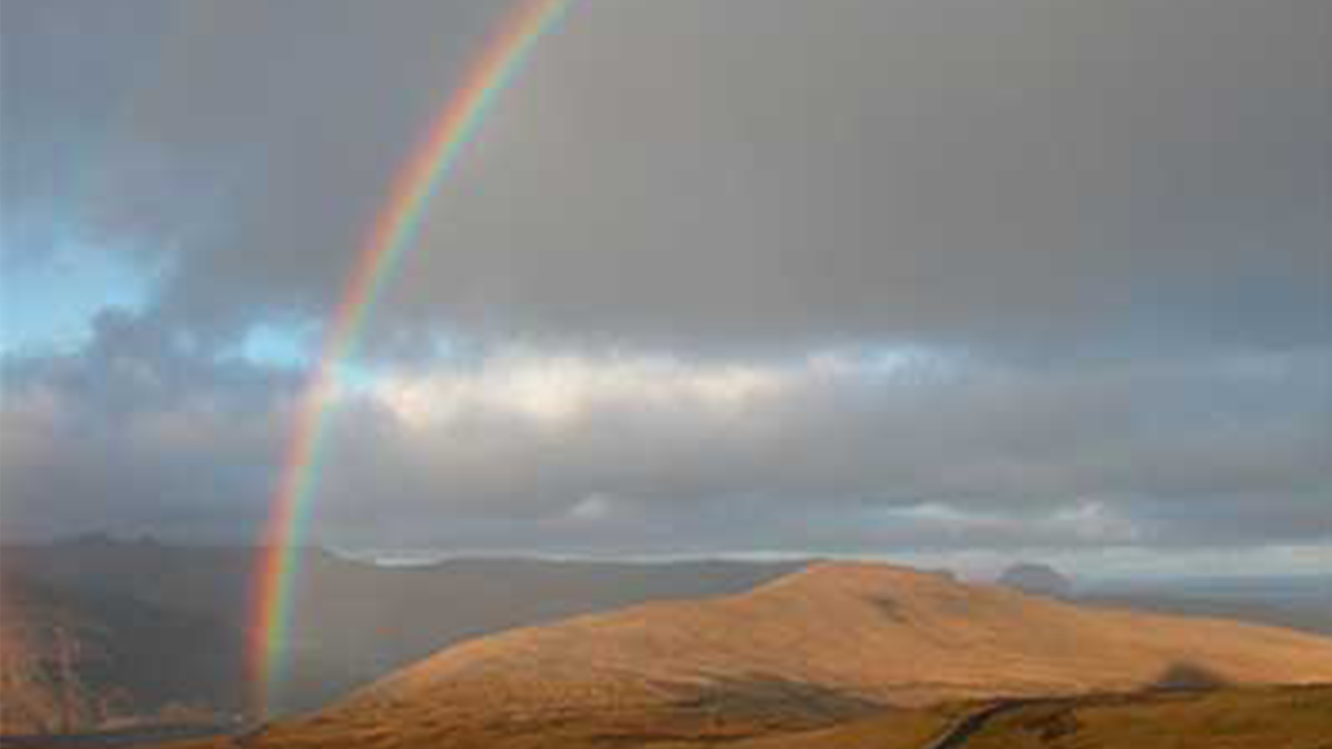 Image of a rainbow seen in the sky over land.
