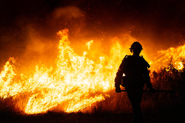 Orange and red fire in the background with a firefighter walking in front of it.