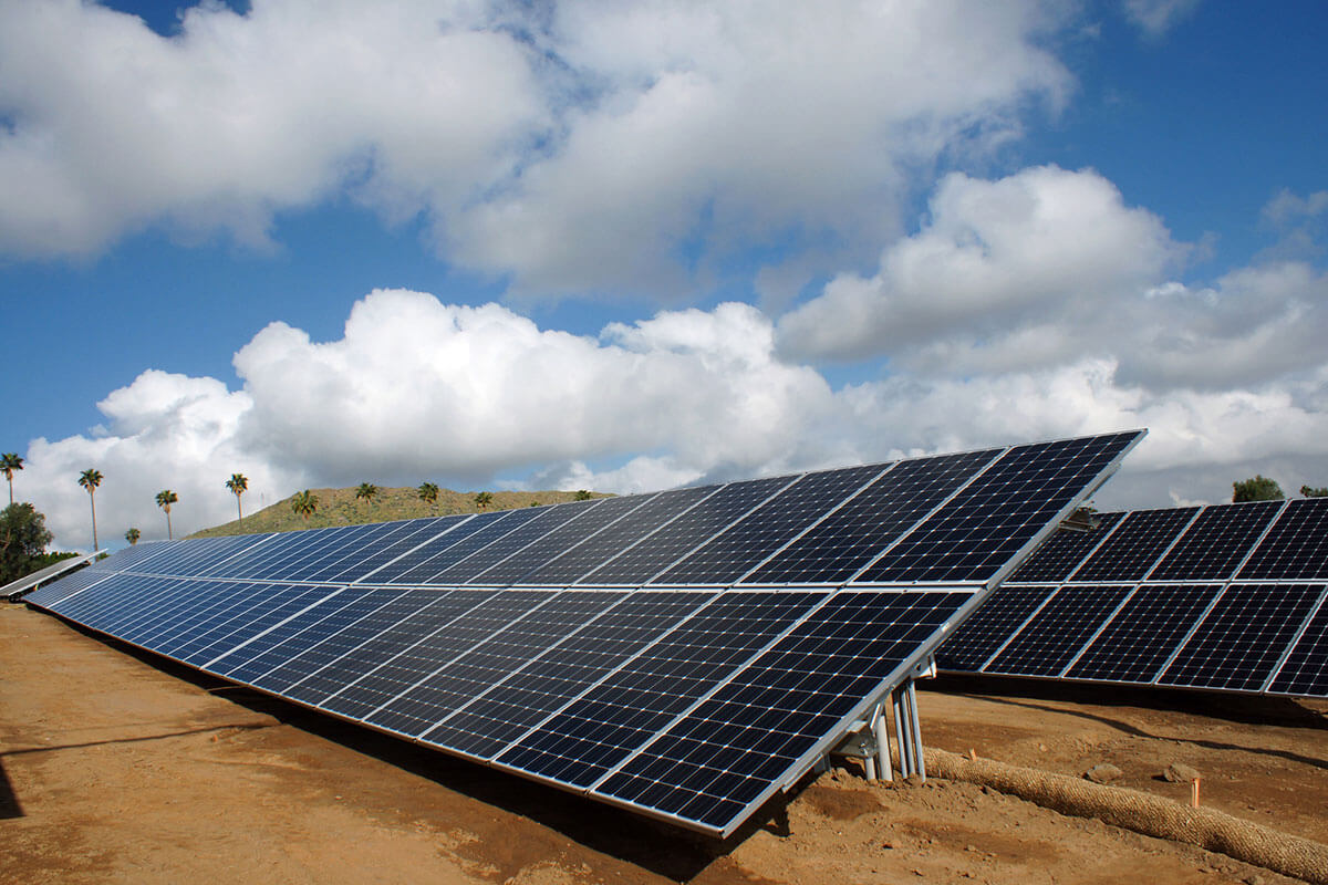 Solar panels on dirt ground under a cloudy sky.