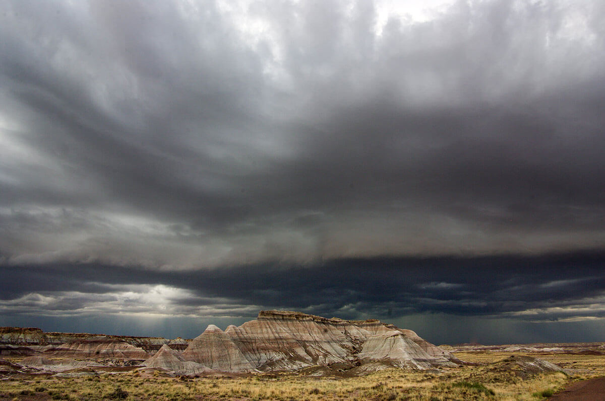 A dark storm cloud fills the sky above a tall, layered rock formation in a field of tall yellow and green grasses.